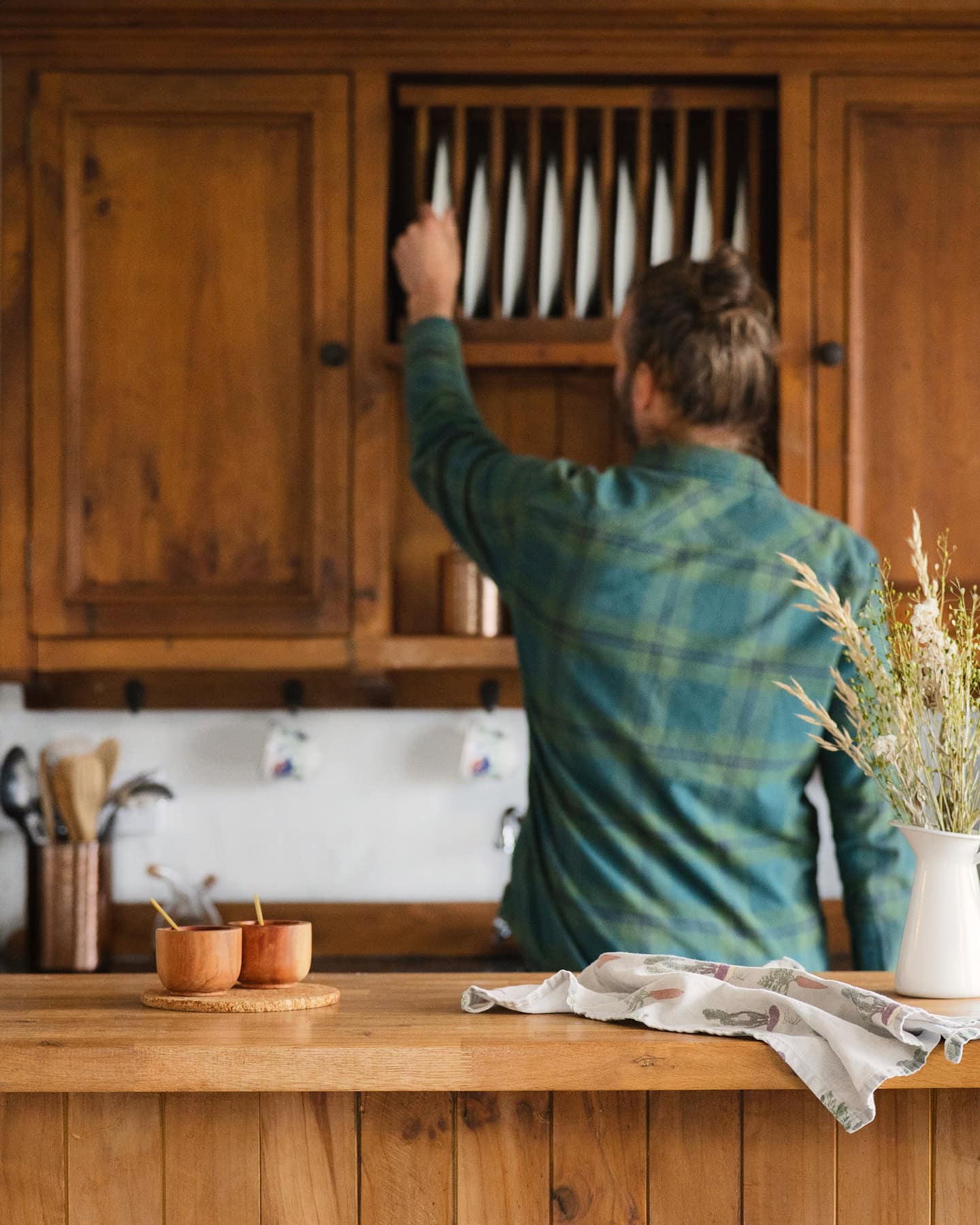 sanctuary-cottages-pipers-cottage-interior-08 Guest reaching for a plate in the rustic wooden kitchen of Pipers Cottage, a cozy holiday rental with countryside charm.
