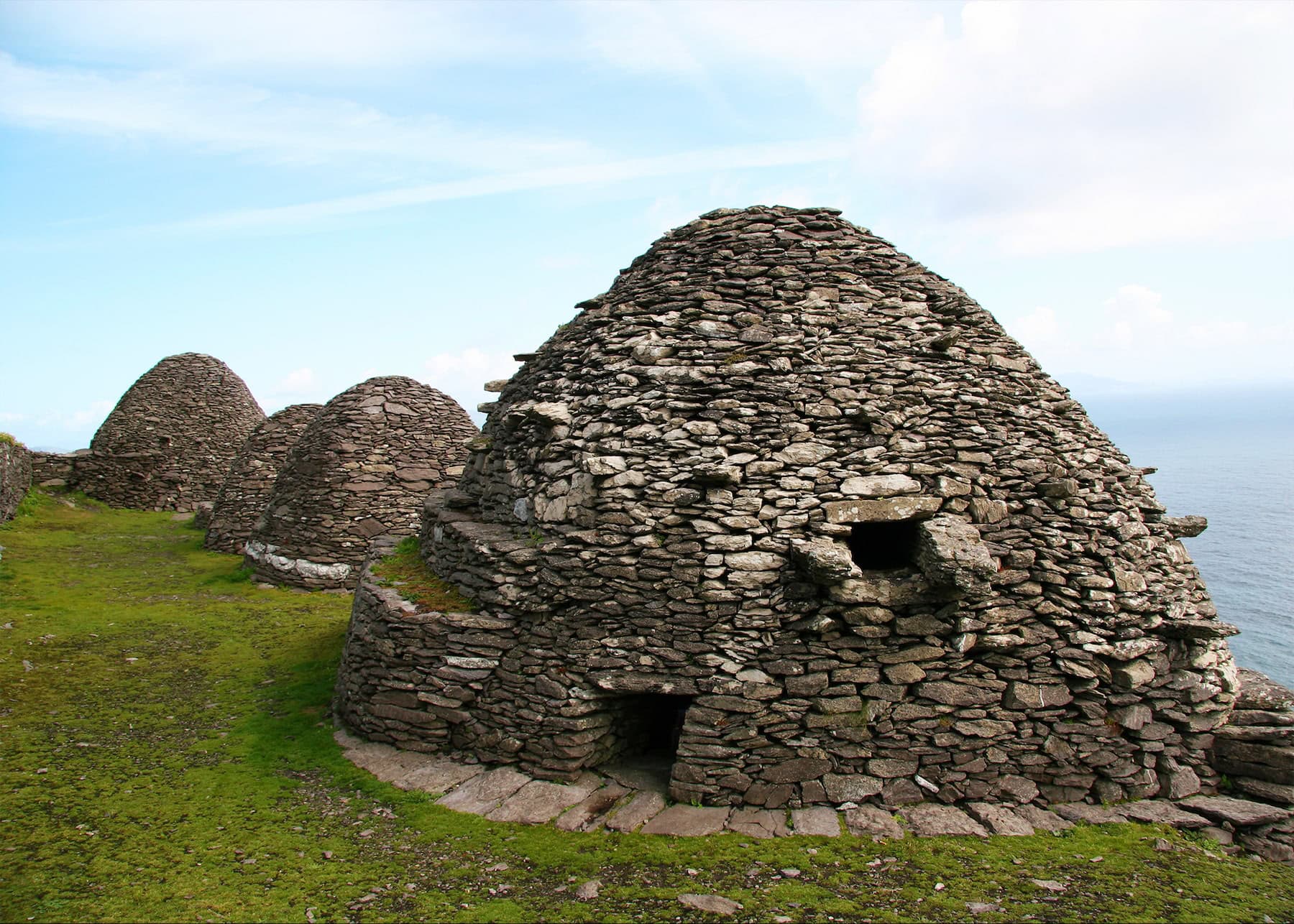 Ancient beehive huts constructed of dry-stone masonry on Skellig Michael, with their distinctive dome shapes arranged in a row overlooking the ocean.