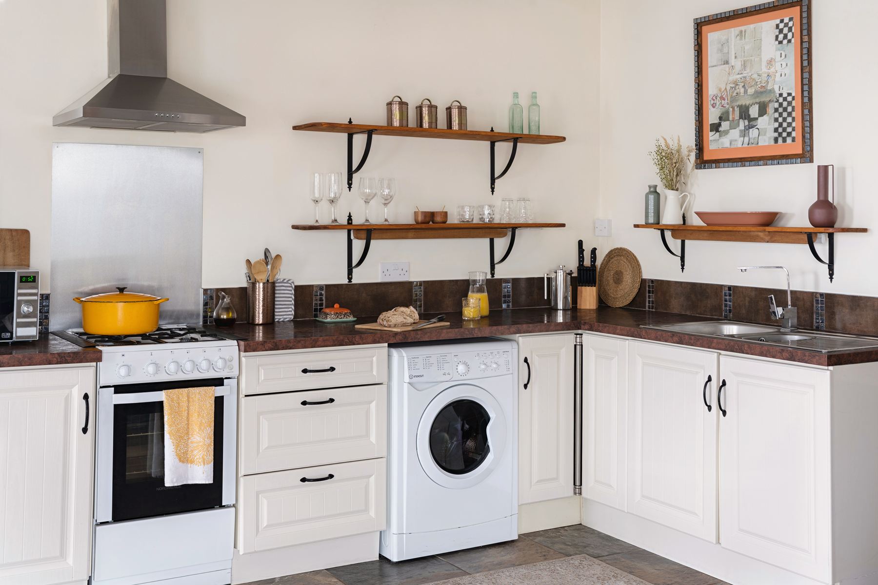 Corner kitchen with cream cabinets, gas cooker, open wooden shelves, and a built-in washing machine in The Studio's open-plan layout.