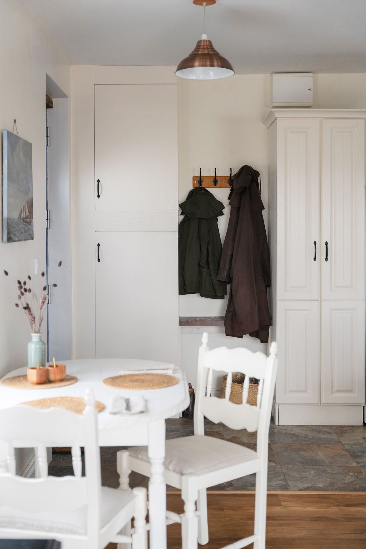 Compact dining space near the front door of The Studio with a coat rack, built-in cupboards, and two chairs set around a small table.