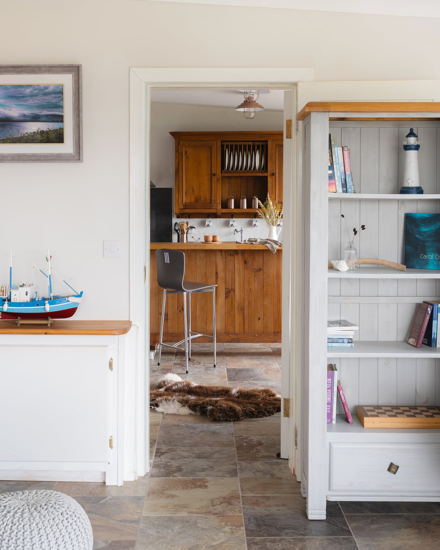 sanctuary-cottages-ocean-blue-group-bookings-1440×1800 View from Ocean Blue’s living room into adjoining Pipers Cottage via connecting door, ideal for group bookings at Sanctuary Cottages in Dingle. Features coastal décor, tiled flooring, and open-plan kitchen cabinetry.