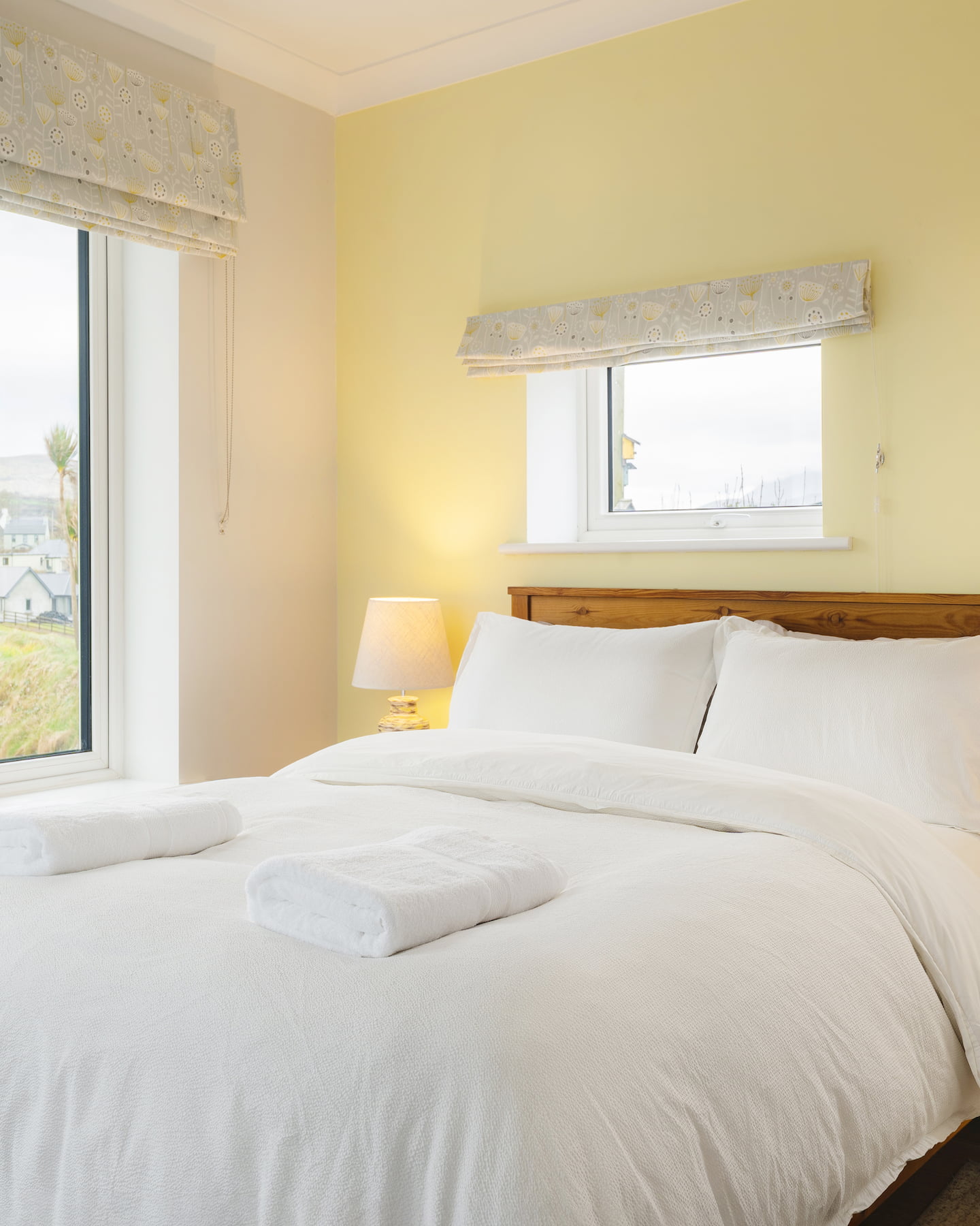 sanctuary-cottages-ocean-blue-master-bedroom-1440×1800 Bright and inviting master bedroom at Ocean Blue, Sanctuary Cottages in Dingle, featuring a crisp white duvet, soft lighting, and dual-aspect windows with views across the bay.